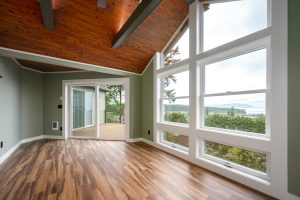 Empty room with large windows showing trees and a bay, light green walls, a wood ceiling, and a sliding glass door that leads to a deck