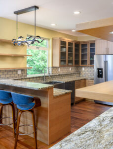 Light kitchen with marbled granite countertops, light wood cabinets, blue stools at the breakfast bar, and a decorative light above the breakfast bar