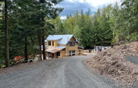 In-progress photo of a large two-story house with large windows and exposed exterior insulation on a heavily wooded lot.
