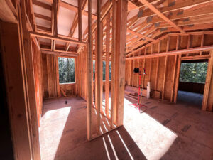 Residential construction site with wooden framing in progress, showing exposed walls and roof structure.