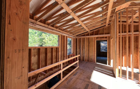 Residential construction site with wooden framing in progress, showing exposed walls and roof structure.