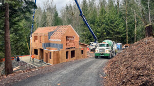 In-progress photo of a framed in two-story home with a concrete truck in the driveway, pouring the concrete patio.