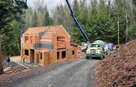 In-progress photo of a framed in two-story home with a concrete truck in the driveway, pouring the concrete patio.