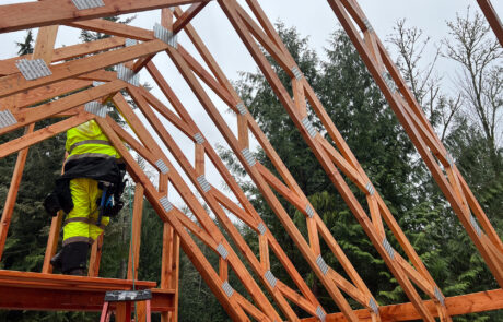 Construction worker in yellow safety suit standing on a wooden scaffolding structure and installing trusses into a residential construction project.