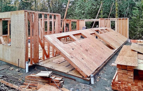 Construction site of partially framed in house and construction workers erecting exterior walls.