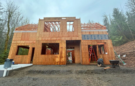 Construction site of a house with partially completed wooden framing, showing exposed walls and roof structure.
